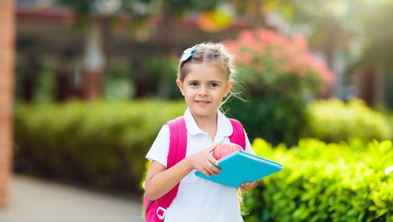 girl walking to school with a backpack on holding an apple and a book