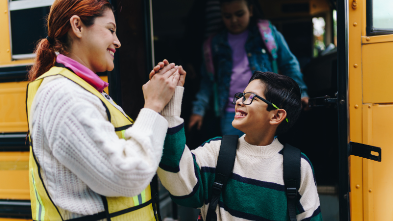 School teacher helping a boy off the school bus, giving him a high five