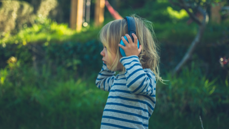 young girl standing outside with ear defenders on to help regulate sounds