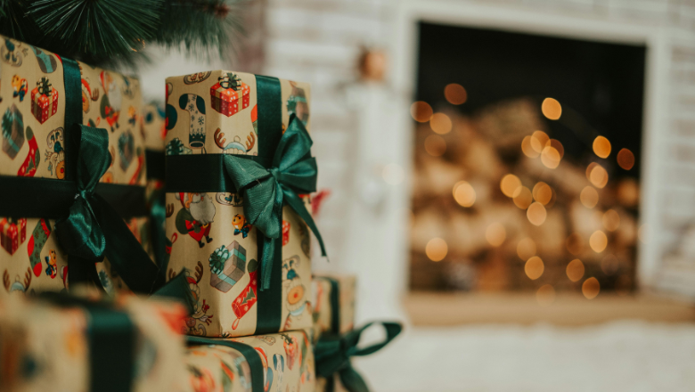 wrapped christmas presents, tied with a green silk bow, sit under the tree which is next to a fireplace